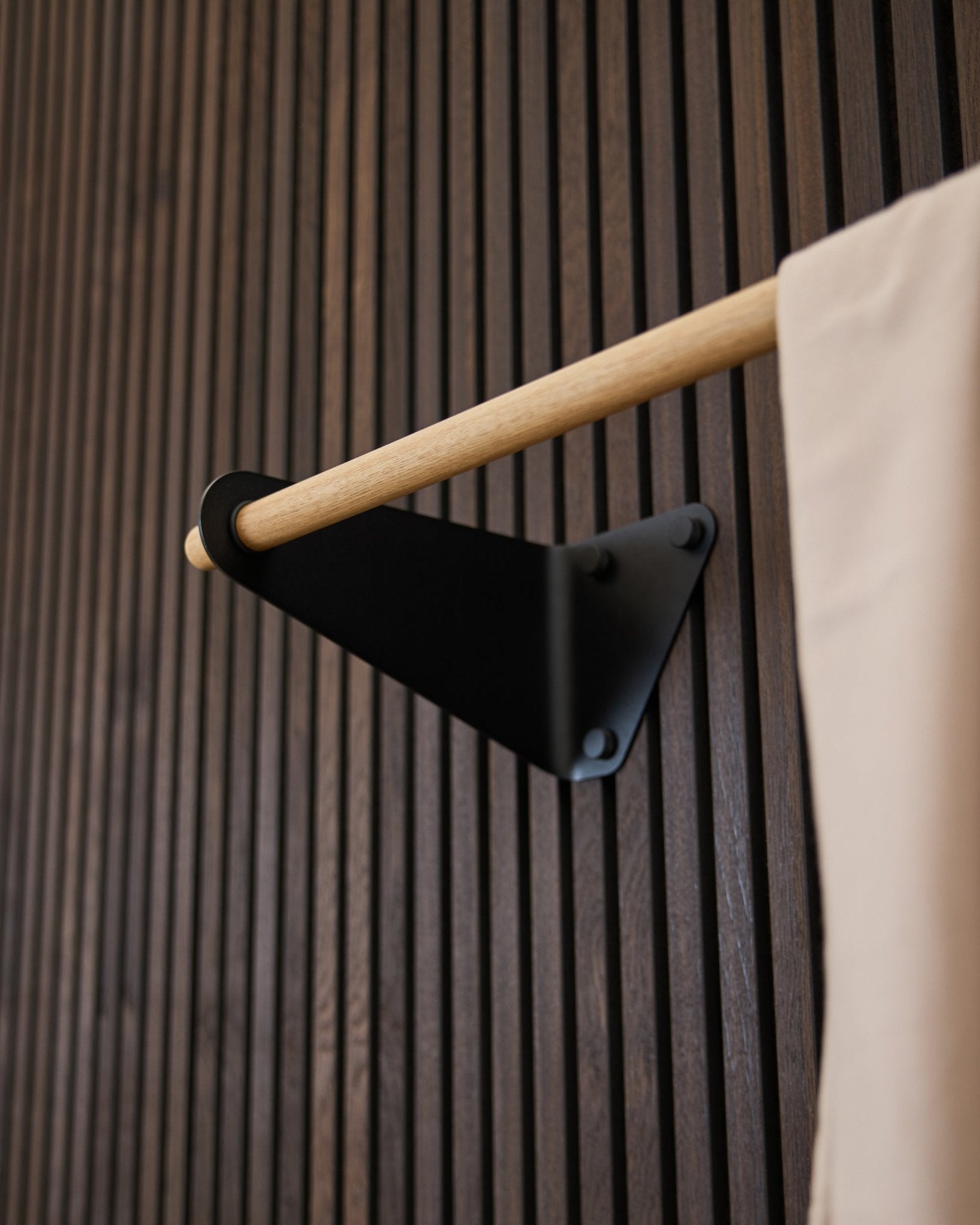 Appendiabiti Linn di WoodUpp in black (115,9 cm) montato su un Pannello acustico Akupanel scuro scanalato, con dettaglio in tessuto beige e staffa black.