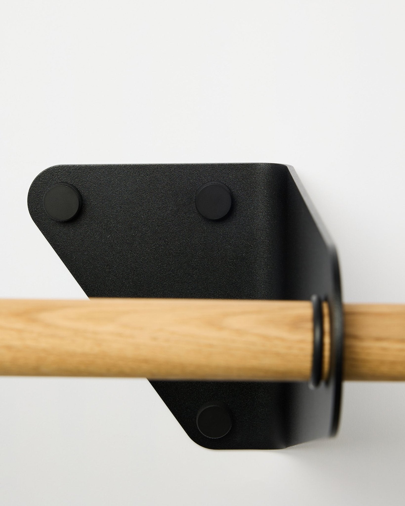 Primo piano dell’appendiabiti WoodUpp Linn in black, 115,9 cm, installato su una parete bianca con una staffa triangolare in metallo, presentato come parte degli accessori acustici nordici.
