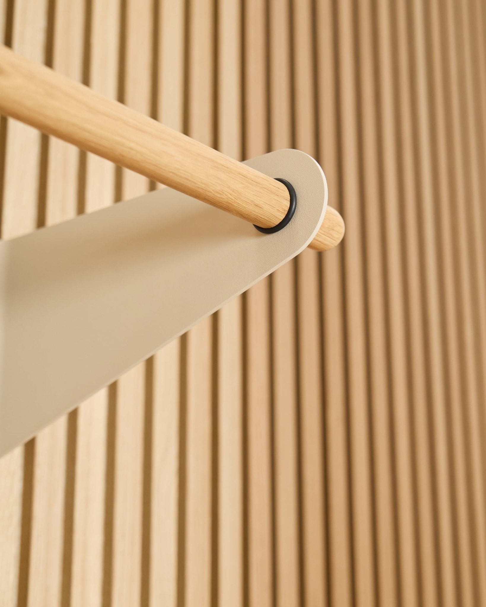 Primo piano dell’appendiabiti Coat Rail WoodUpp Linn in beige (75,9 cm), montato su una staffa in metallo beige davanti a un pannello acustico a doghe Akupanel dalla superficie materica.