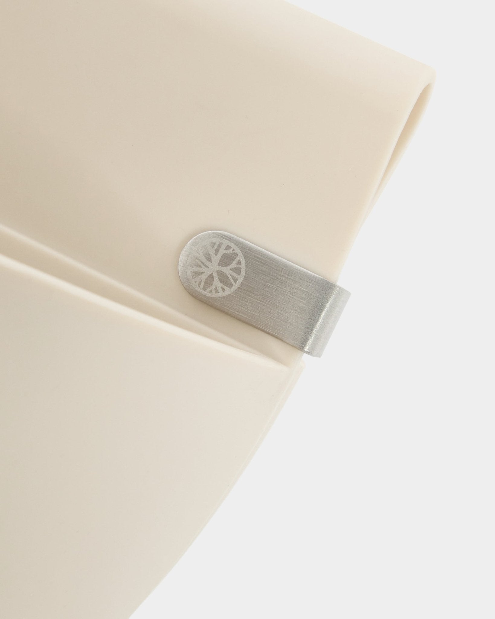Primo piano di un pannello WoodUpp Gro | Soft Pocket / BM2 (4 l) in beige chiaro, con clip in metallo e dettaglio circolare inciso, su uno sfondo bianco semplice.