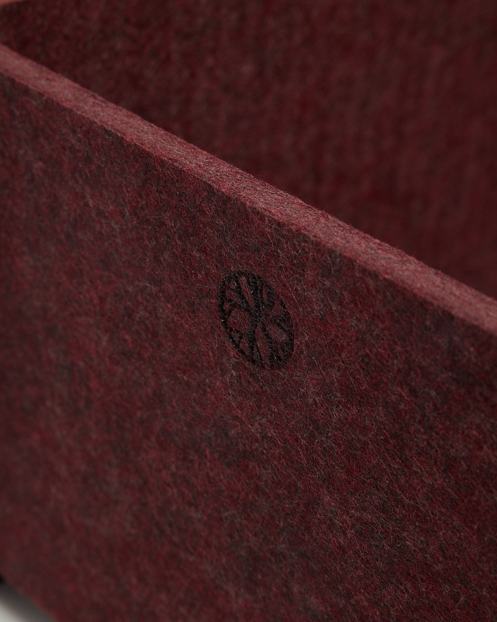 Primo piano di WoodUpp Vigg | Felt Box / BM2 in ox red, che mostra il feltro PET testurizzato e un emblema circolare black nell'angolo. Design di accessori acustici nordico.