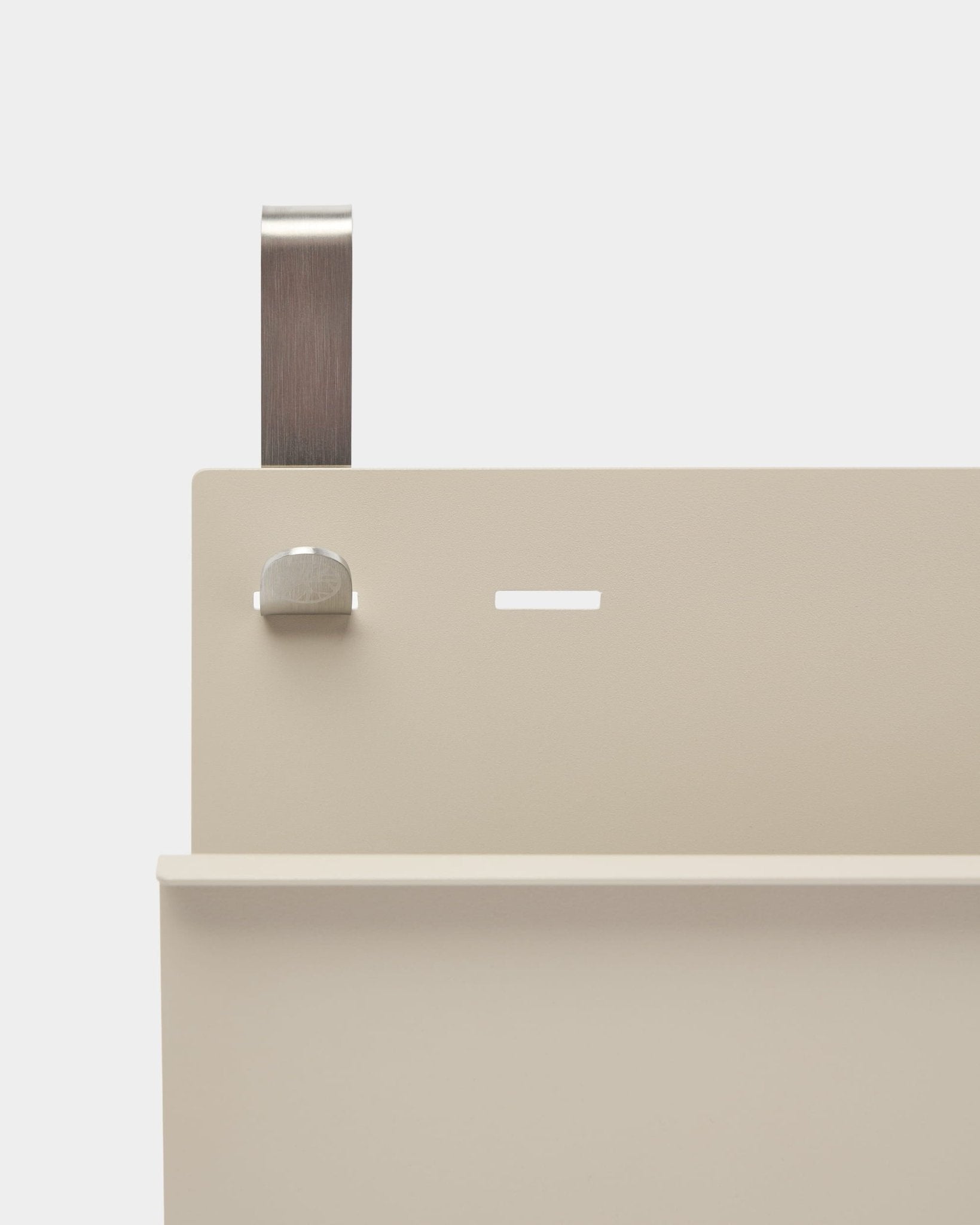 Primo piano del portariviste Nell di WoodUpp in beige, con struttura in steel verniciata a polvere, mensola, scanalatura, bullone e maniglia curva; funziona come divisorio per ambienti o portariviste.
