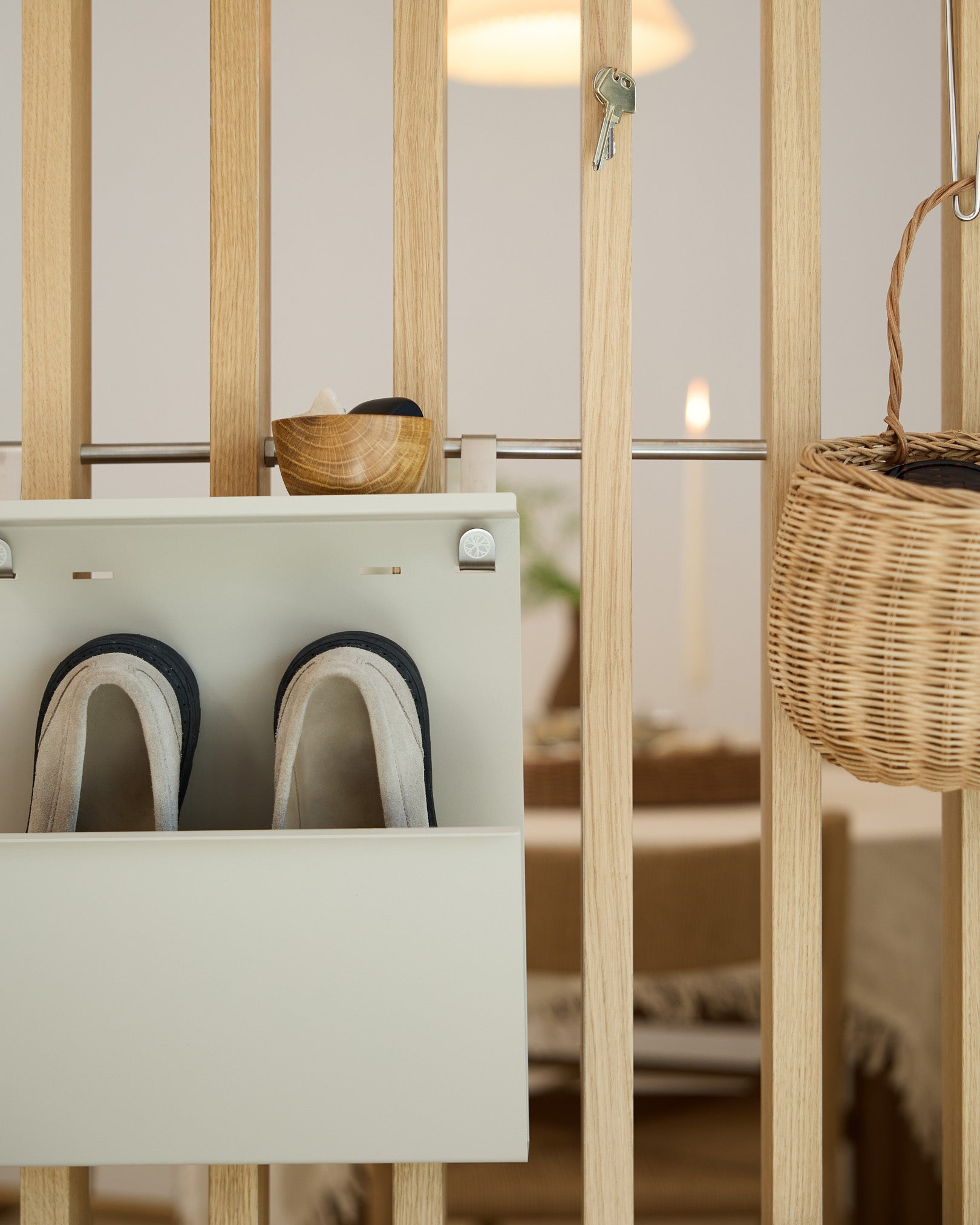 WoodUpp Nell Beige Shoe Storage ospita pantofole, una ciotola e un cesto in vimini su un divisorio in legno; sullo sfondo si vede la zona pranzo.