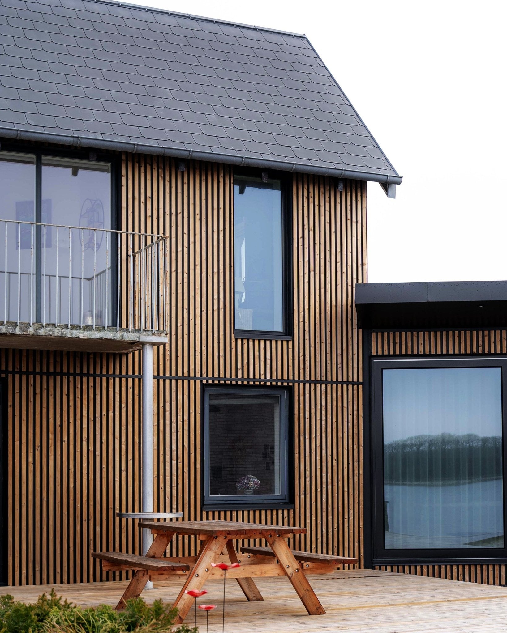 Casa moderna con pannelli per facciata WoodUpp Aluwood in Brown oliato, con finestre large, un balcone e una terrazza con tavolo da picnic in legno.