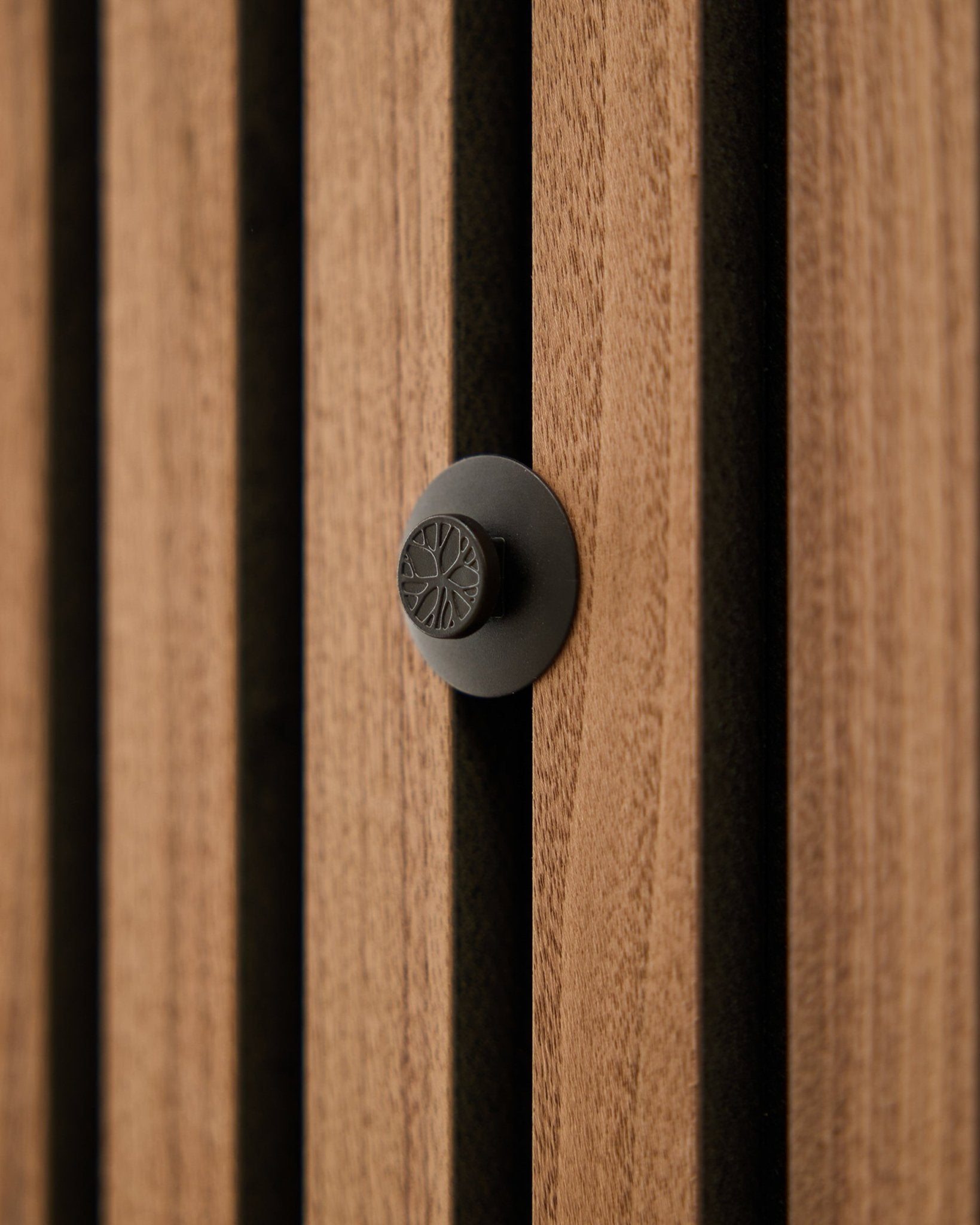 Primo piano di un pomello rotondo black del set WoodUpp Dupps Original, installato su una moderna parete acustica a listelli in legno vertical Akupanel.