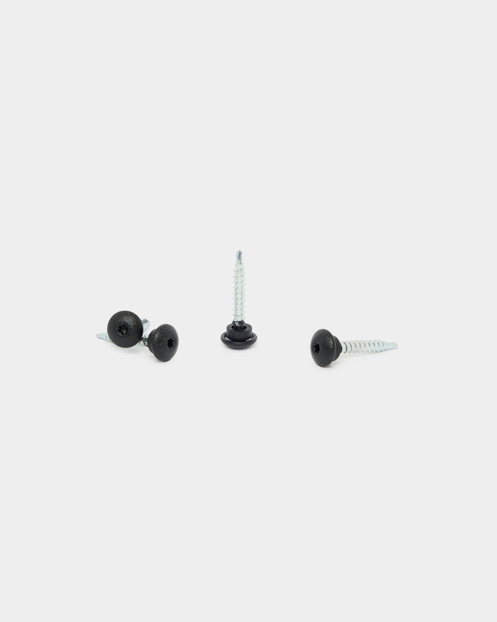 Tre viti WoodUpp 4,8x35 black con rondelle Ø9,5 su sfondo bianco, pensate come elementi di fissaggio per i pannelli da facciata per esterni Aluwood.