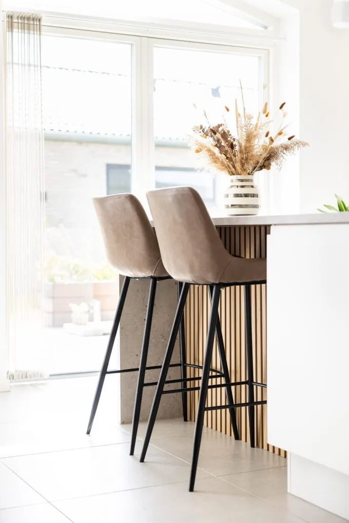Sgabelli da bar beige su unisola della cucina con un vaso di fiori secchi, grandi finestre e stile nordico contemporaneo con pannelli acustici alle pareti.