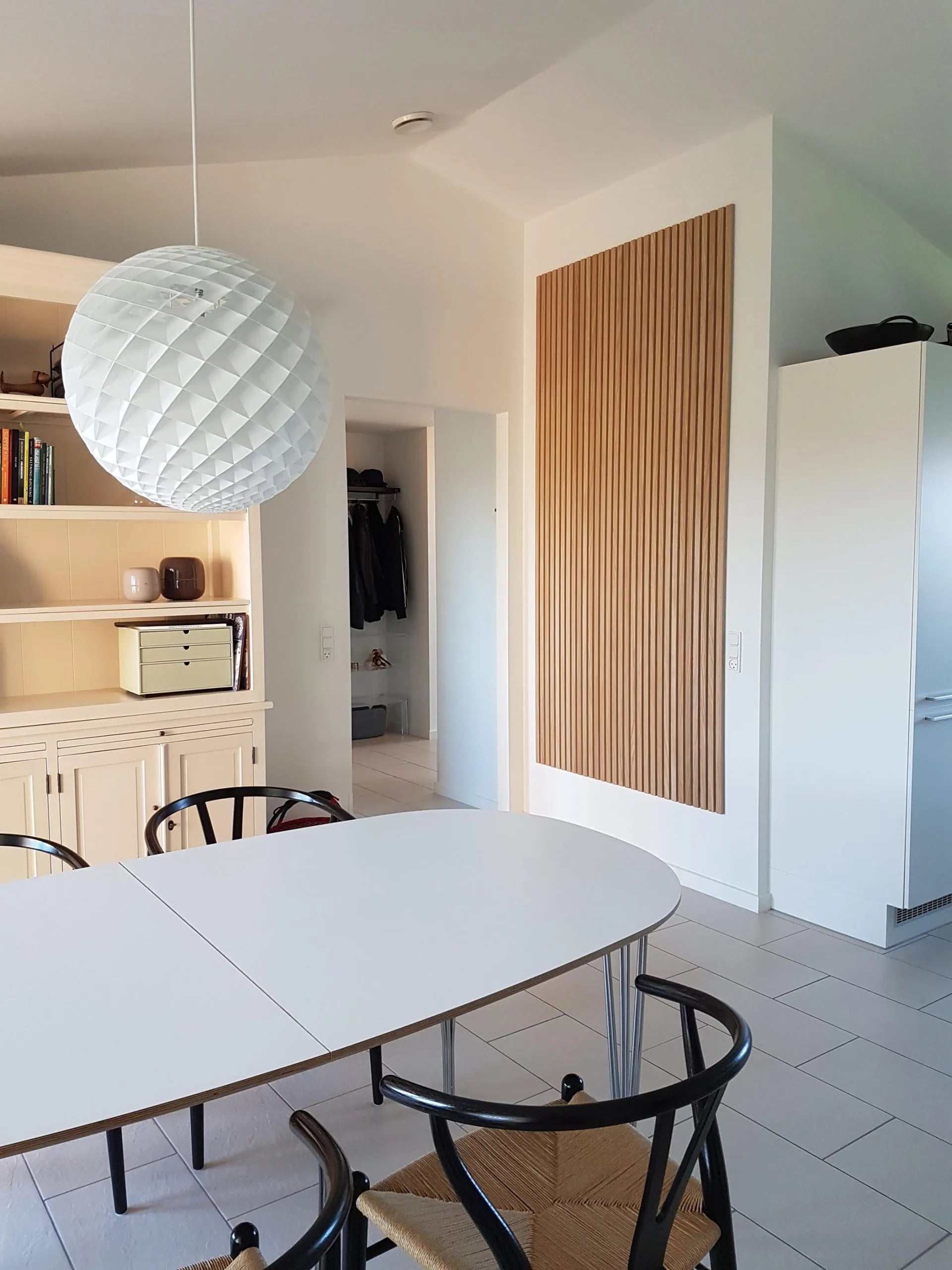 Moderna zona pranzo con tavolo ovale bianco, sedie nere, grande lampada a sospensione testurizzata e mobile acustico Akupanel in legno chiaro.