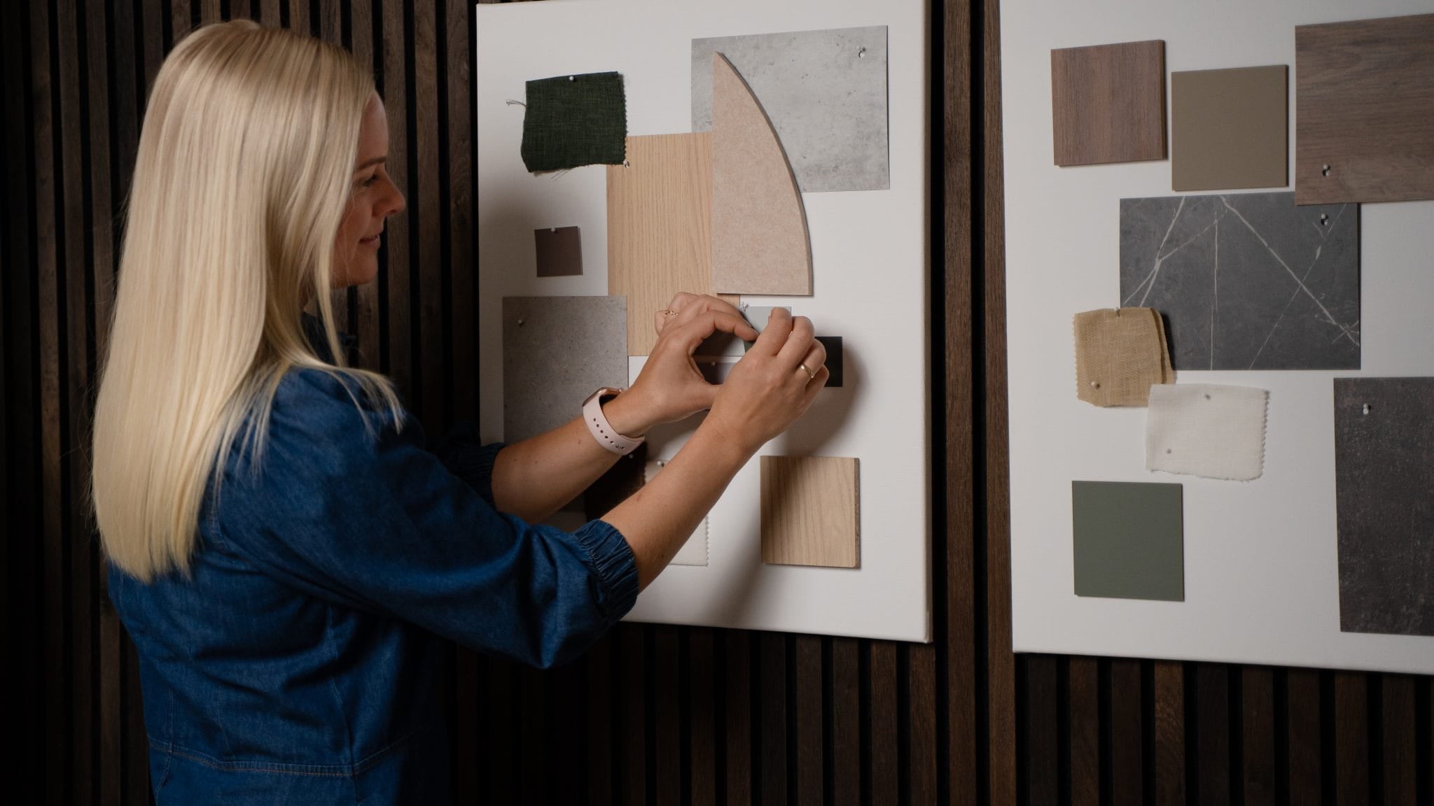 Una donna dispone campioni di tessuto e di colore su una lavagna, con accanto unaltra lavagna dispirazione, vicino a pannelli acustici in legno della collezione Akupanel di WoodUpp.