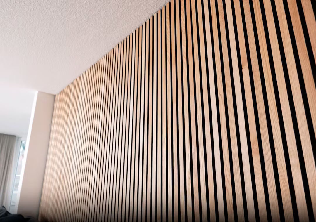 Primo piano del pannello acustico in legno Akupanel a doghe verticali con motivo a strisce, installato su una parete interna sotto un soffitto bianco.