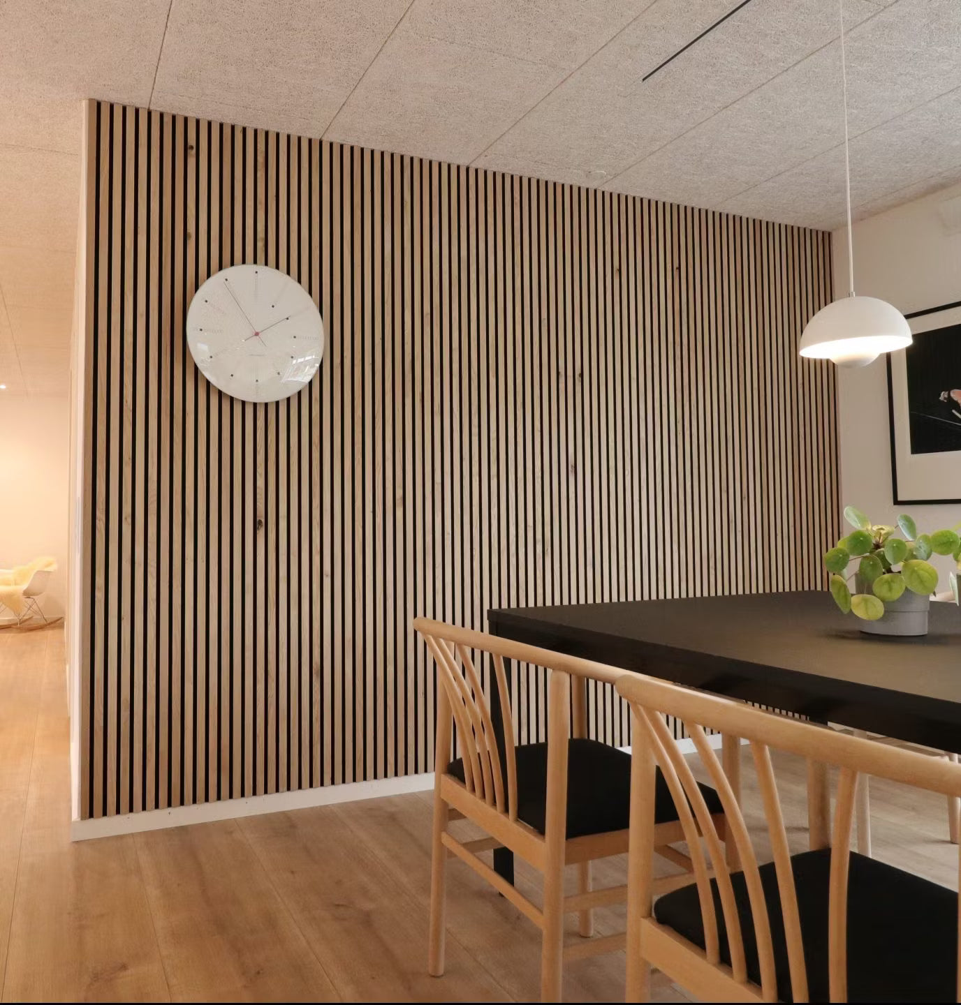 Sala da pranzo moderna con parete a doghe in legno acustico nordico Akupanel, tavolo nero, sedie in legno con sedute nere e centrotavola con piante in vaso.