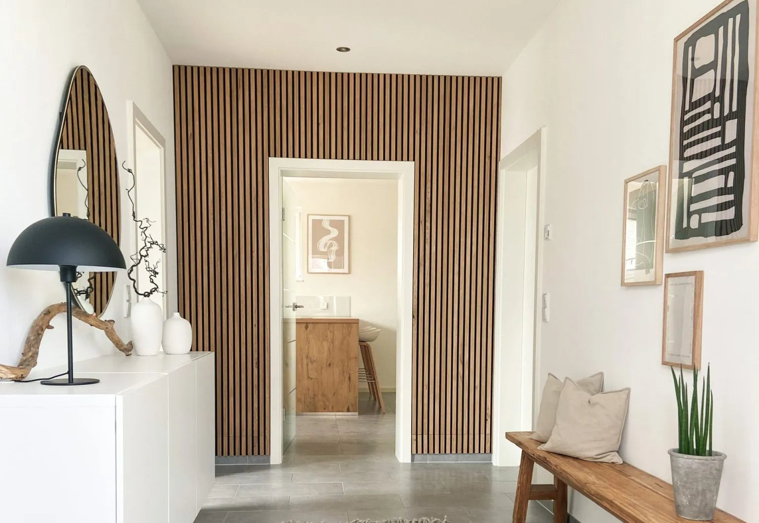 Un corridoio moderno con una parete acustica a doghe di legno nordico Akupanel, pareti bianche, una panca imbottita e un arredamento minimalista.