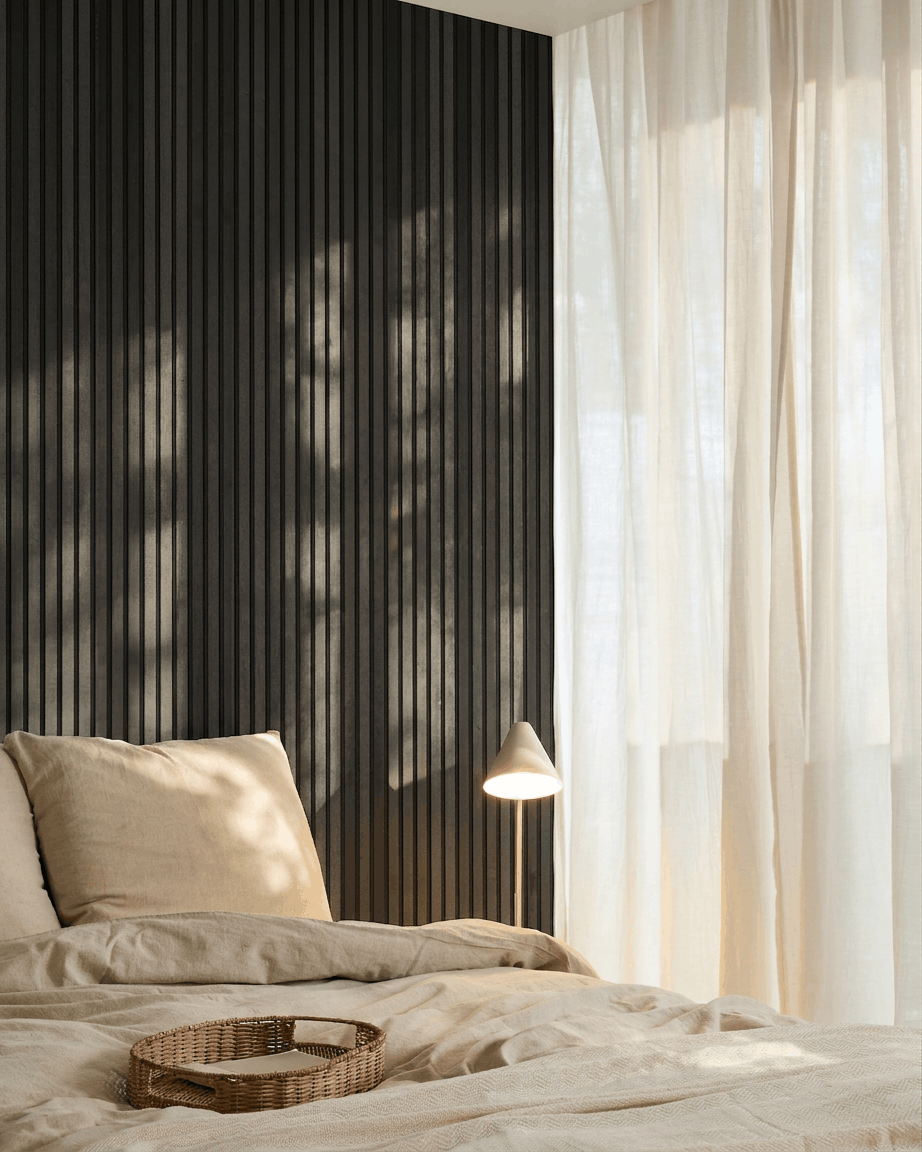 Camera da letto nordica minimalista con un WoodUpp Akupanel Pannello acustico in Black Ash, biancheria da letto beige, un vassoio in vimini e tende velate che lasciano entrare la luce naturale.