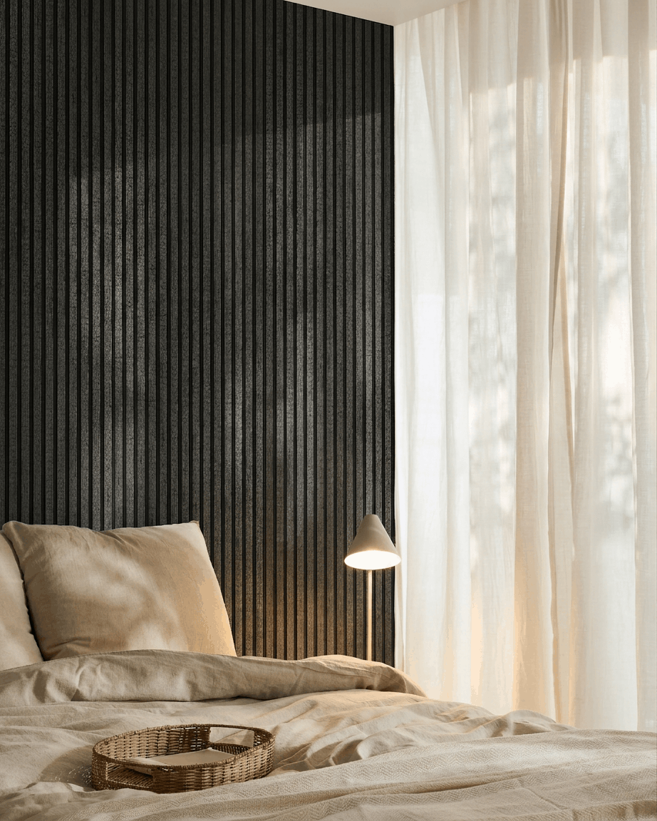 Accogliente camera da letto con biancheria da letto beige, un vassoio in rattan, una lampada bianca, tende leggere e un pannello acustico in legno WoodUpp Akupanel charcoal montato a parete.