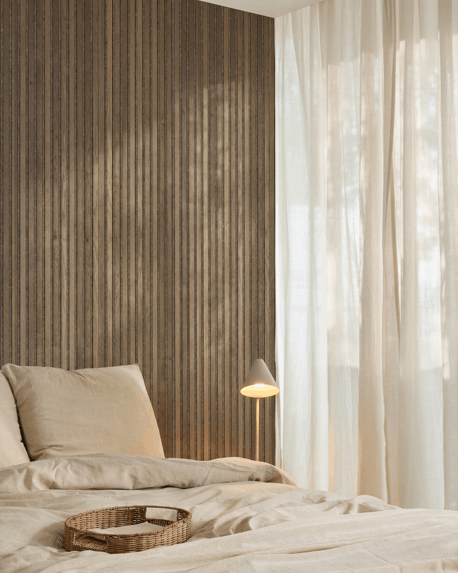 Camera da letto minimalista con biancheria da letto beige, un vassoio in vimini, un pannello acustico a doghe WoodUpp Akupanel Rustic Grey Oak, una lampada bianca e tende leggere.