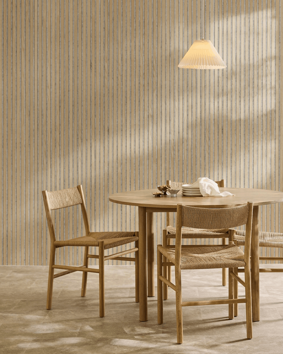 Zona pranzo minimalista con tavolo rotondo in legno, sedie intrecciate, lampada a sospensione e un pannello acustico in legno WoodUpp Akupanel in Classic Rovere con feltro grey.