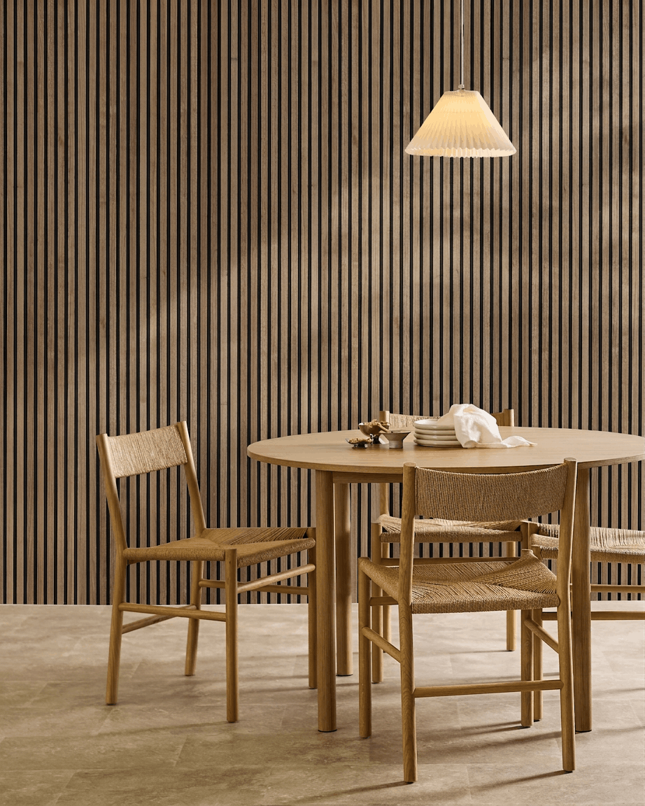 Zona pranzo minimalista con tavolo rotondo, sedie intrecciate, lampada a sospensione e un pannello acustico in legno WoodUpp Akupanel in Natural Wood con feltro black sulla parete.