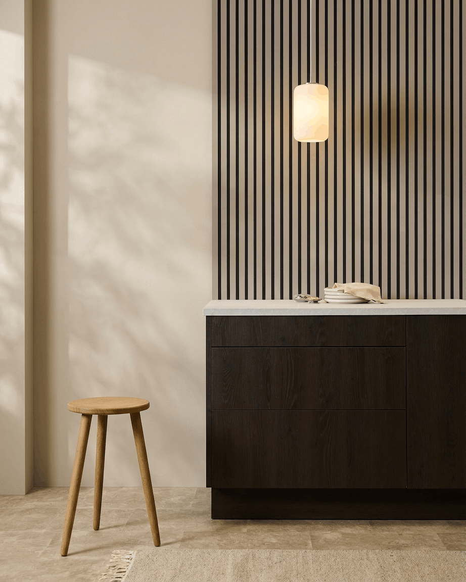 Cucina minimalista con pannelli acustici WoodUpp Akupanel (Stone, felt Black) sulla parete, sgabello in legno, mobili scuri e lampada a sospensione in tonalità neutre.