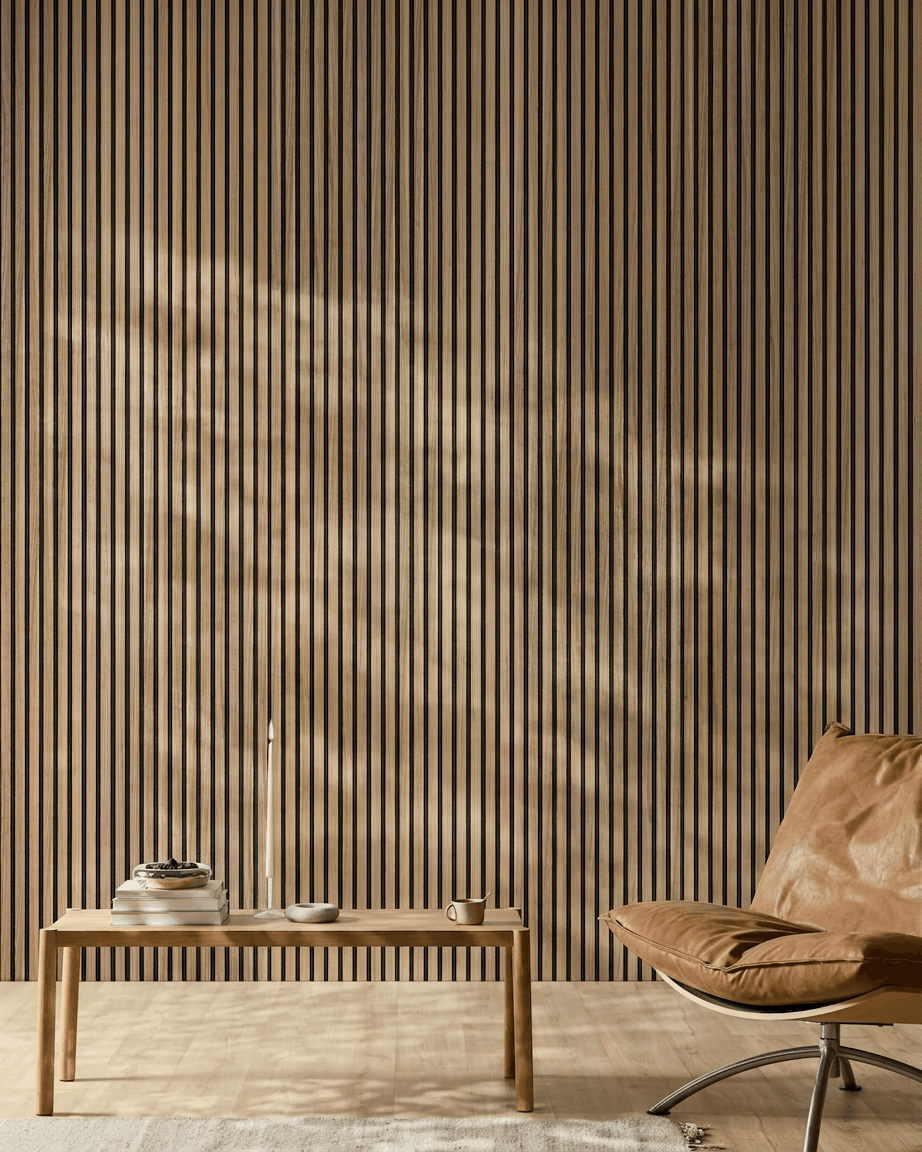 Interno minimalista ambiente con un pannello WoodUpp Akupanel Pannello acustico (listelli English Walnut doghe, feltro black), sedia in pelle color cuoio, tavolo in legno chiaro, candela, libri, tazza e tappeto bianco alla luce del sole.