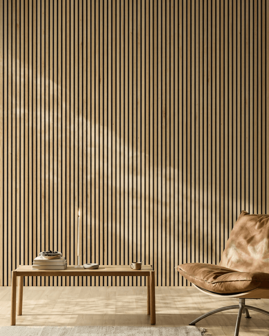 La luce del sole illumina un moderno ambiente con un Akupanel Pannello acustico di WoodUpp in Rustic Natural Oak sulla parete, accanto a una sedia in pelle color cuoio e a una panca minimalista.