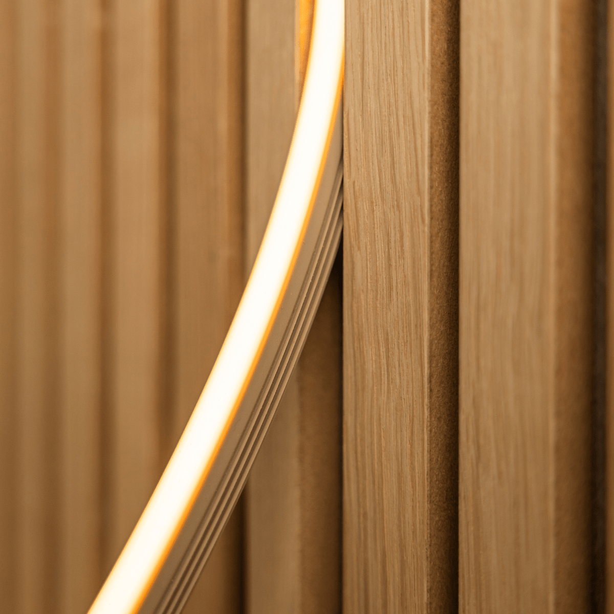 Primo piano della striscia LED WoodUpp Lumi in beige (240 cm) che diffonde una luce gialla calda sulle doghe in legno acustiche Akupanel vertical; compatibile con Philips Hue.