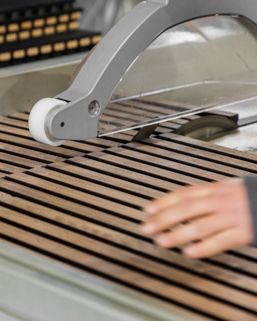Una mano usa i precisi Cutting service di WoodUpp per rifilare le doghe Pannello acustico a spaziatura uniforme, garantendo un allineamento accurato per l’installazione di una parete in legno nordico.