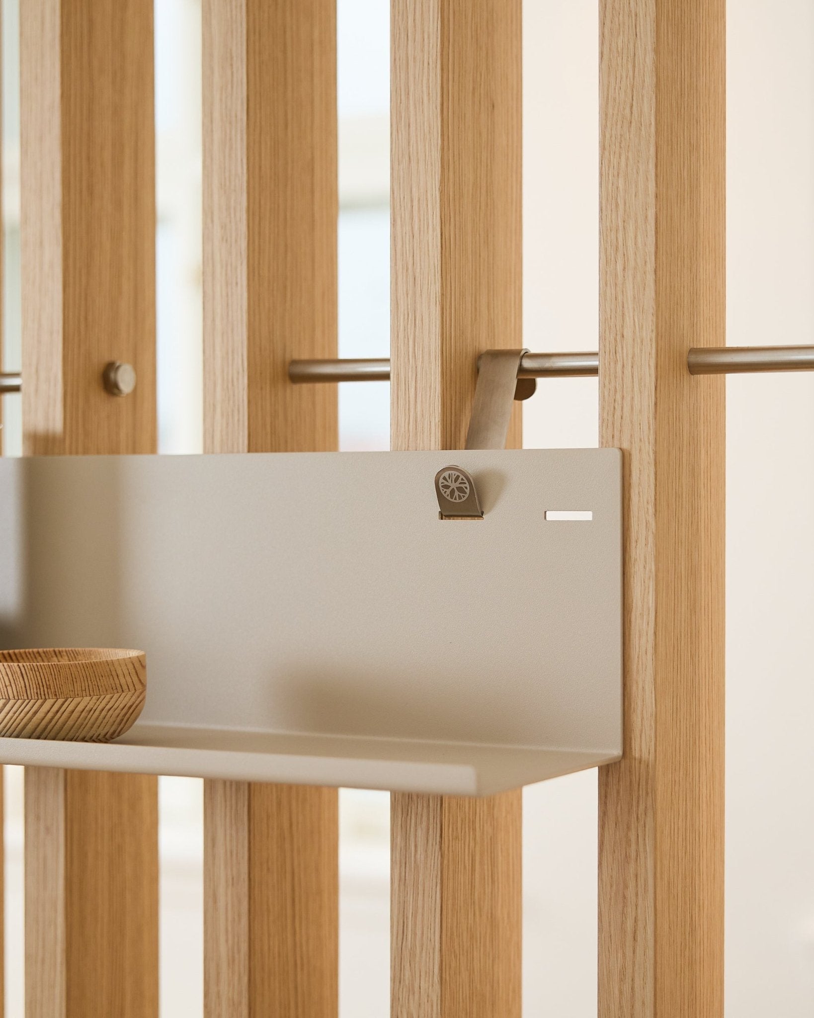 Mensola metallica WoodUpp BM1 Beige (63x13,4 cm) montata su un pannello acustico a listelli vertical, con una ciotola in legno sul lato sinistro della mensola.