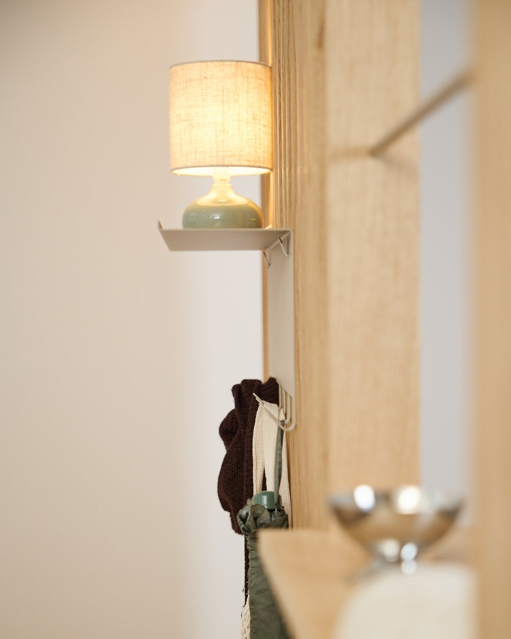 Un appendiabiti WoodUpp Nell BM1 beige (63,5 x 24 cm) si trova sotto una lampada da tavolo small, accanto a una parete in legno chiaro nordico Pannello acustico.