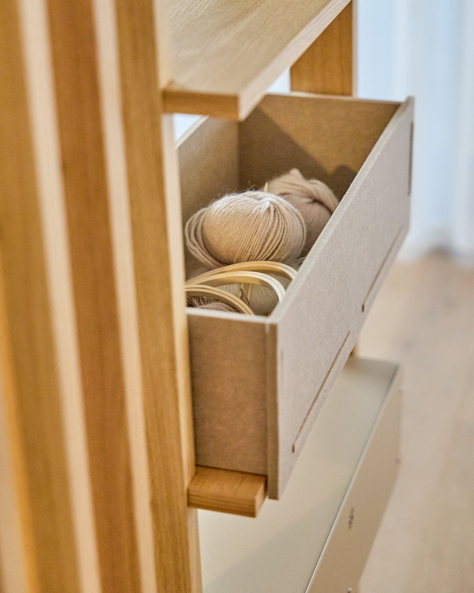 La WoodUpp Vigg Felt Box / BM2 in beige contiene gomitoli leggeri e telai da ricamo in legno su una mensola in legno, in armonia con i pannelli acustici nordici.