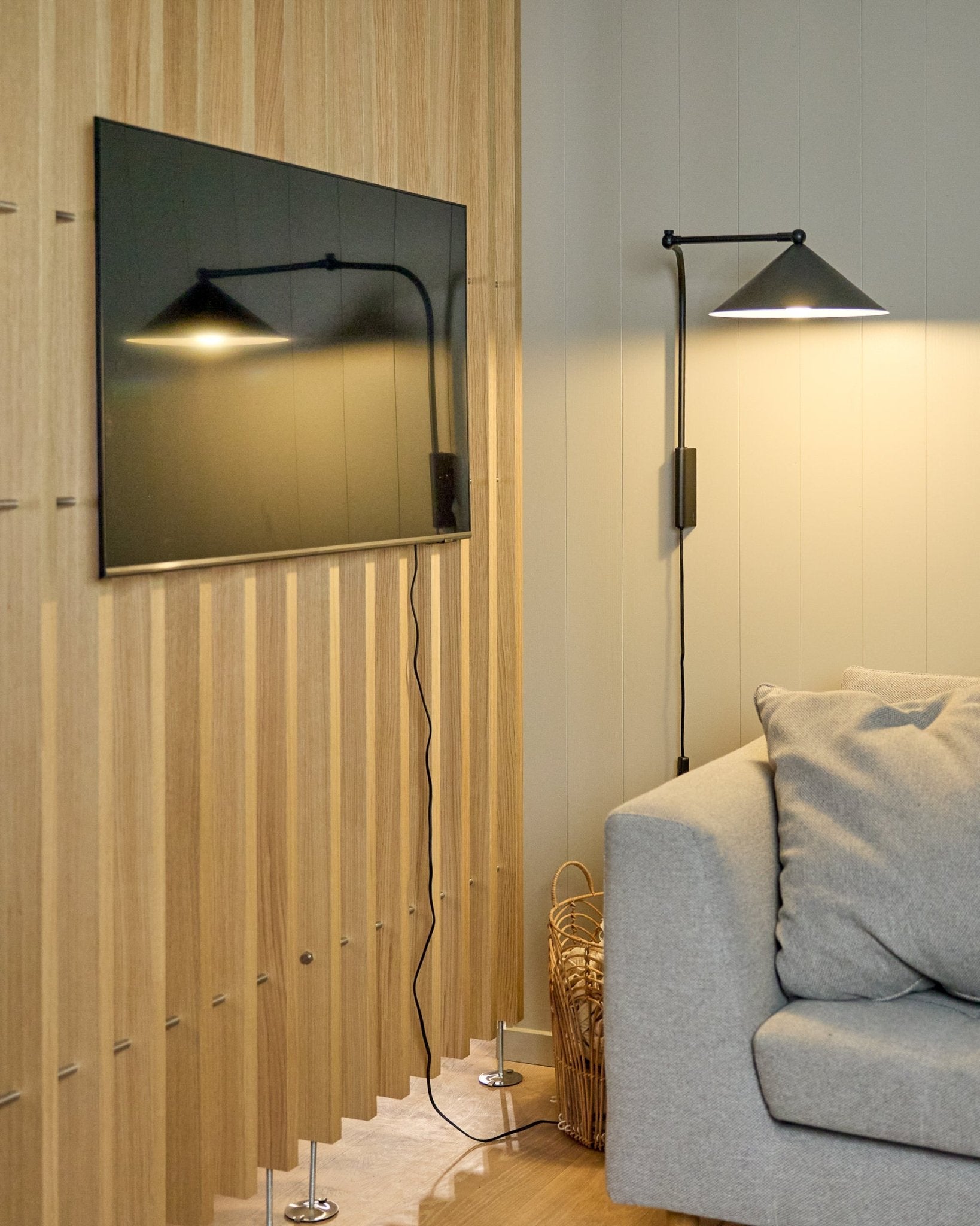 Un Nell | TV-Mount / BM1 di WoodUpp (Beige, 64x44 cm) fissa una TV a schermo piatto su un Pannello acustico nordico accanto a un divano grigio; cestino nelle vicinanze.