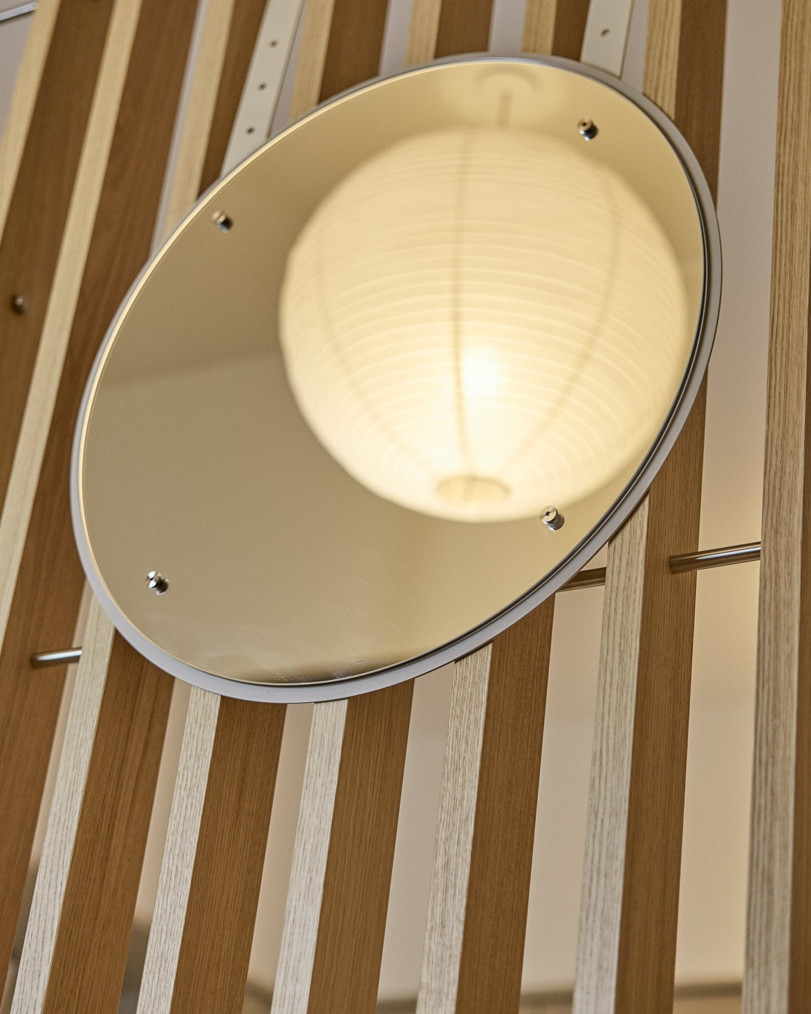 Il Vala | Mirror / BM1, D54 cm di WoodUpp è uno specchio rotondo regolabile in altezza, montato su pannelli acustici a listelli vertical, che riflette una lanterna di carta illuminata.