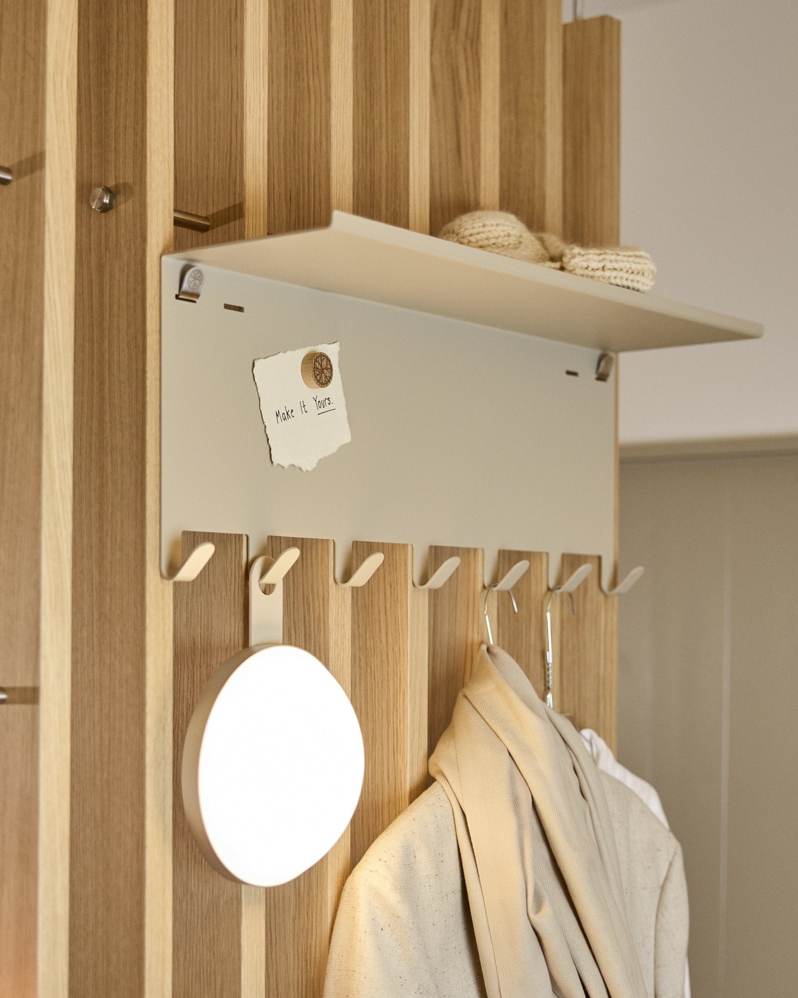 WoodUpp Nell | Appendiabiti BM1 in beige (63,5 x 24 cm), con ganci steel e una mensola con capi in maglia e un biglietto con la scritta embrace BM1.