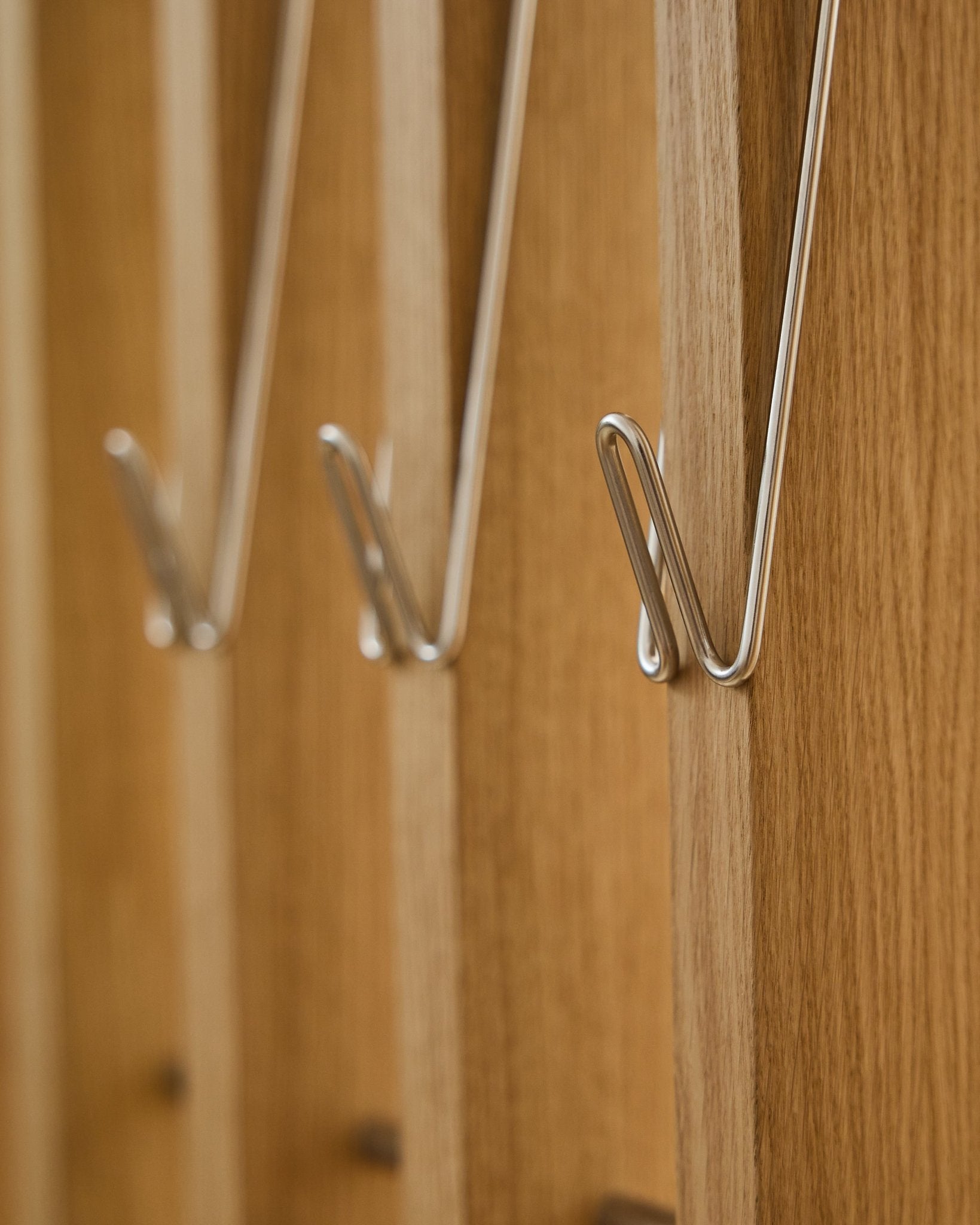 Primo piano di tre Alva | Wire Hook / BM1, acciaio inox Steel, lunghi, di WoodUpp, montati in fila su pannelli acustici in legno Akupanel e con morbide ombre proiettate.