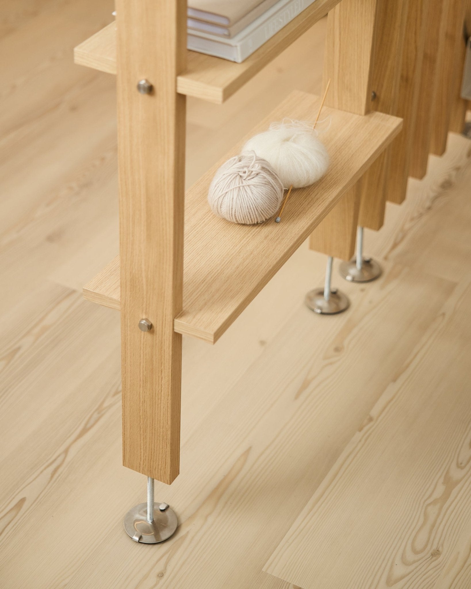 La Lova | Mensola in legno / BM2 di WoodUpp in impiallacciatura Rovere (65,8x20 cm), con filato e ferri da maglia sul ripiano inferiore, su un pavimento in legno chiaro con piedini in metallo.