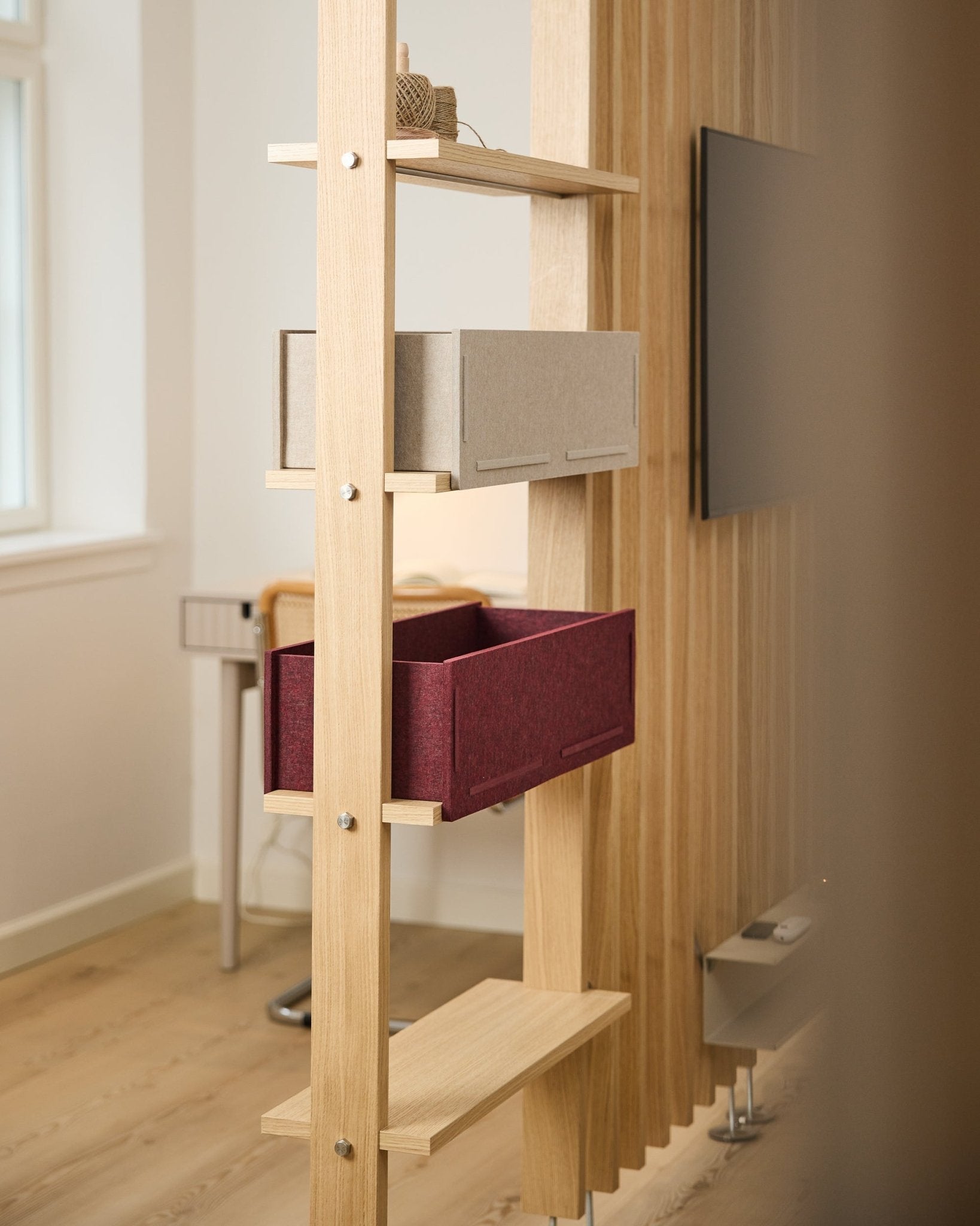 Una mensola WoodUpp presenta un contenitore beige e un ox red Vigg Felt Box / BM2 in una stanza nordica luminosa e minimalista con dettagli acustici in legno.