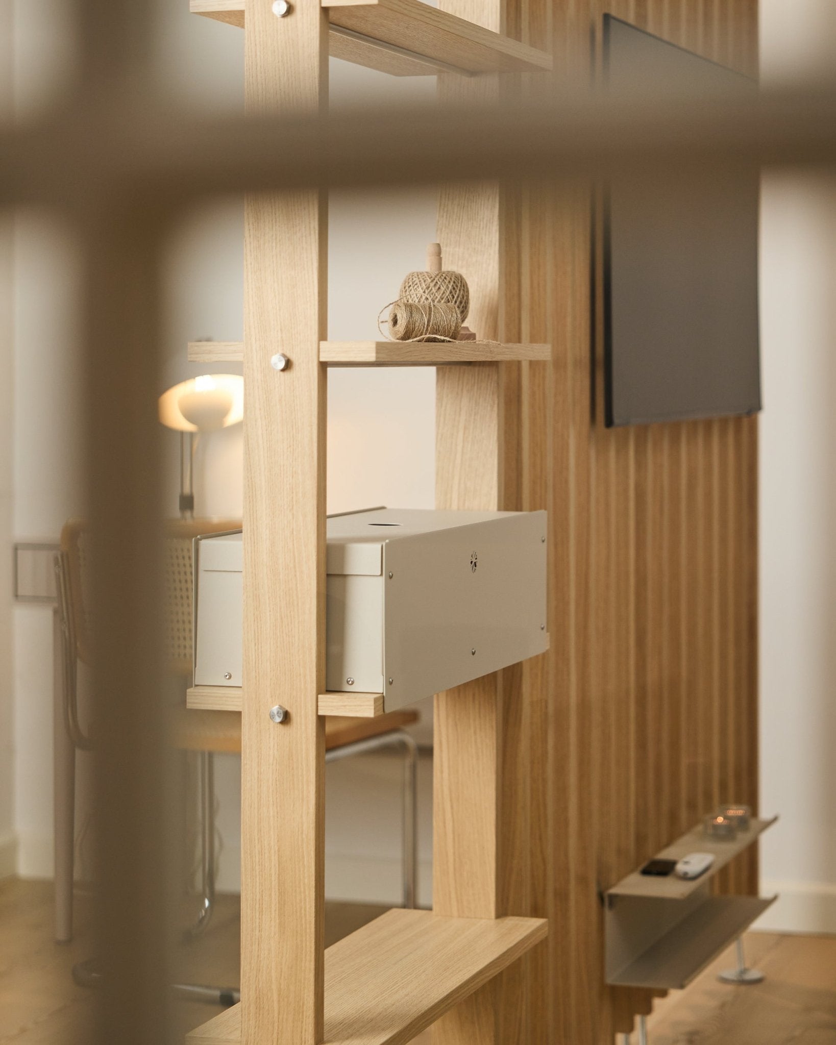 Una stanza accogliente con una sedia, una lampada e una TV mette in risalto la mensola Nell | Metal Box / BM2 di WoodUpp, rifinita in beige, con un arredo nordico essenziale.