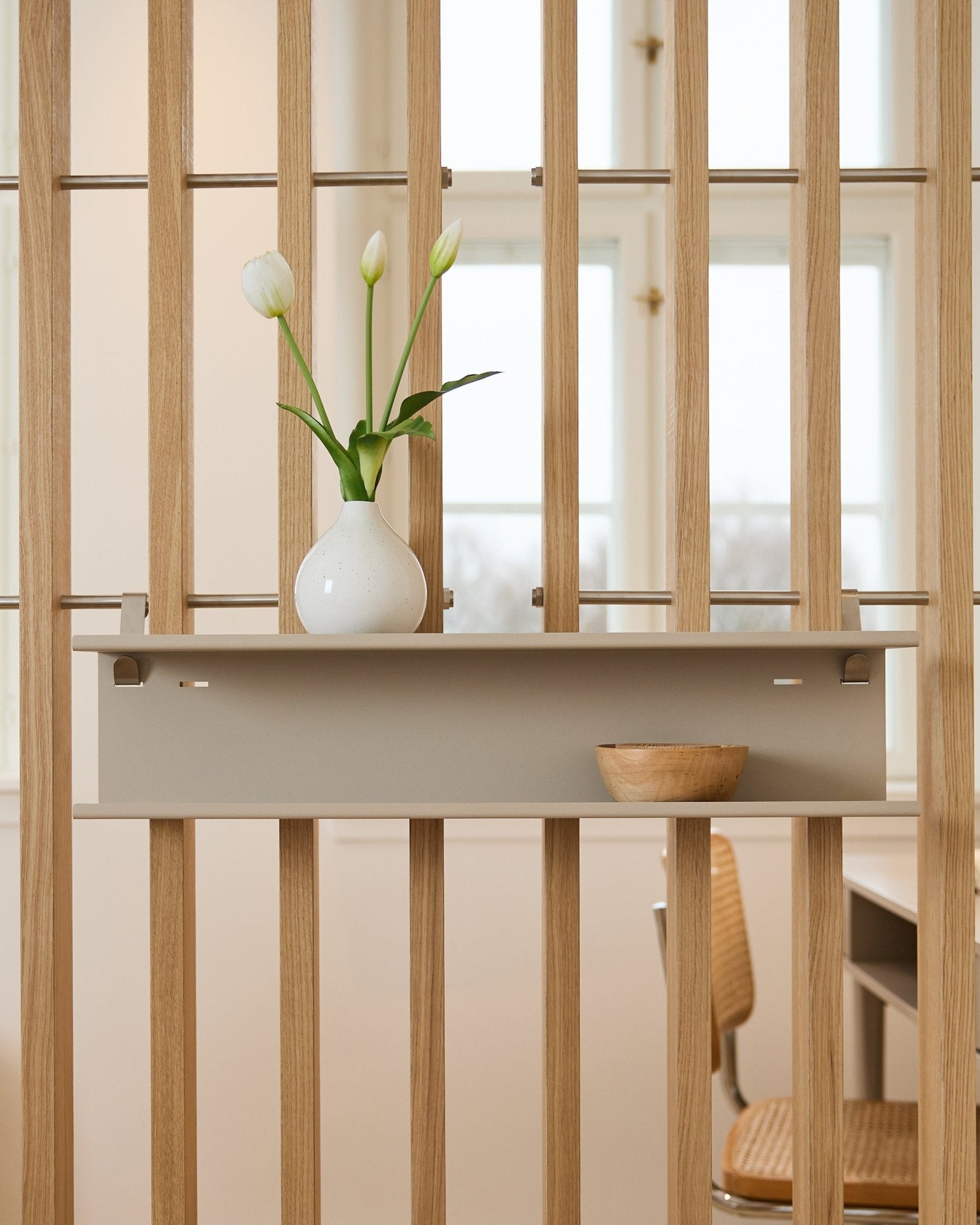 Double Metal Shelf / BM1 di WoodUpp in beige (63,5 cm) montato su un divisorio a listelli, con un vaso e una ciotola in legno.