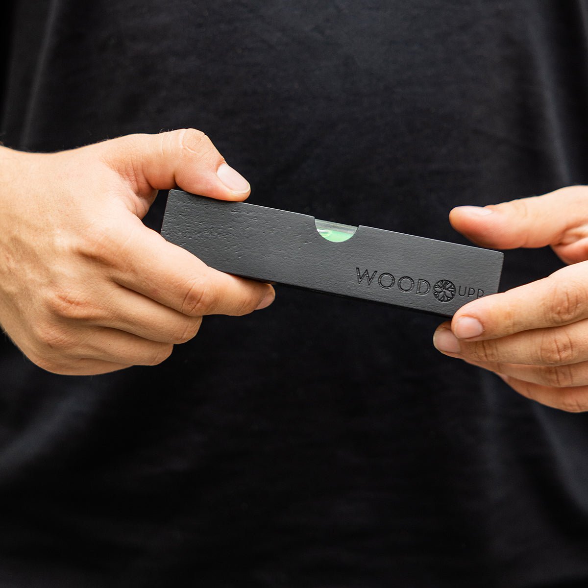 Una persona con una maglia black tiene in mano una livella a bolla WoodUpp black (15 x 3,2 cm), progettata per l’installazione precisa dei pannelli acustici.